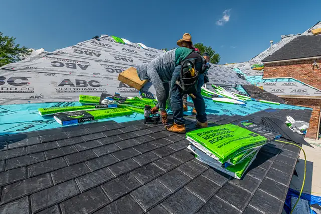 Roofer fastening new composite shingles over synthetic underlayment during a full roof replacement on a Kent, WA home